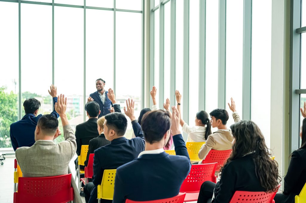 Grupo de personas en un Evento Corporativo Empresarial o Seminario de formación gratuito en donde están levantando la mano.