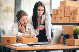 Mujeres propietarias de pequeñas empresas emergentes que utilizan ordenadores y teléfonos en el trabajo con cajas alrededor.