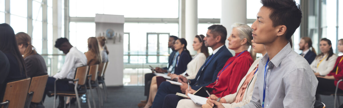charlas-para-empresarios-2 Grupo ejecutivo participa en charlas para empresarios, tomando notas en salón iluminado con ventanales y sillas alineadas.
