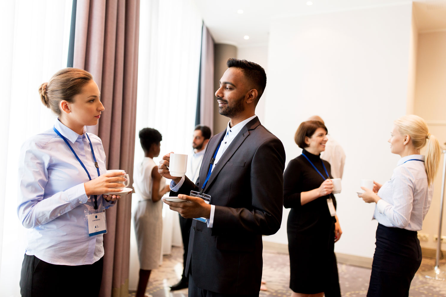 Un hombre de negocios y una mujer joven conversan sonriendo, ambos con acreditaciones, en un networking profesional.