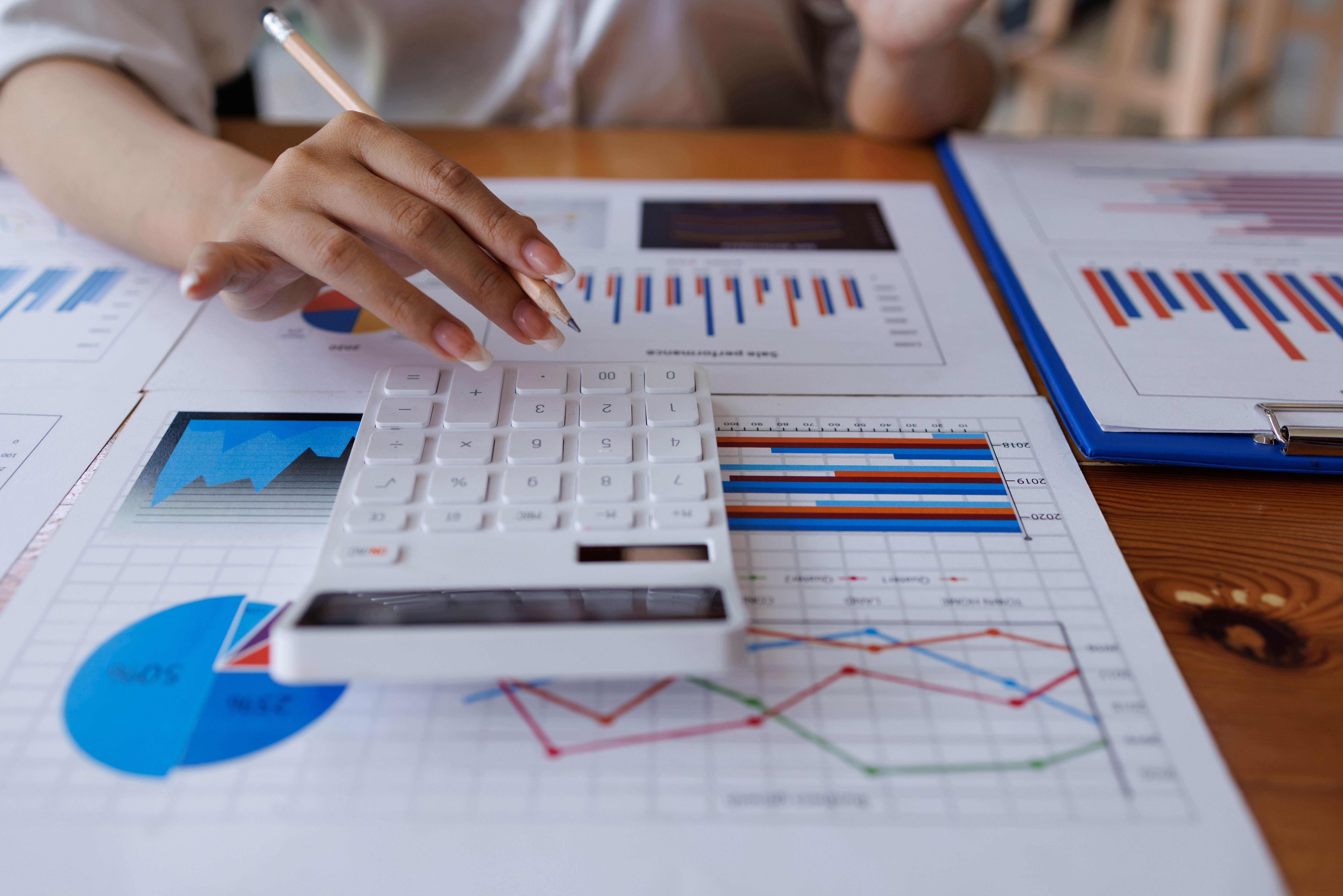 Manos de contadora utilizando calculadora blanca para validar cifras en proyecciones financieras y balances de costos.