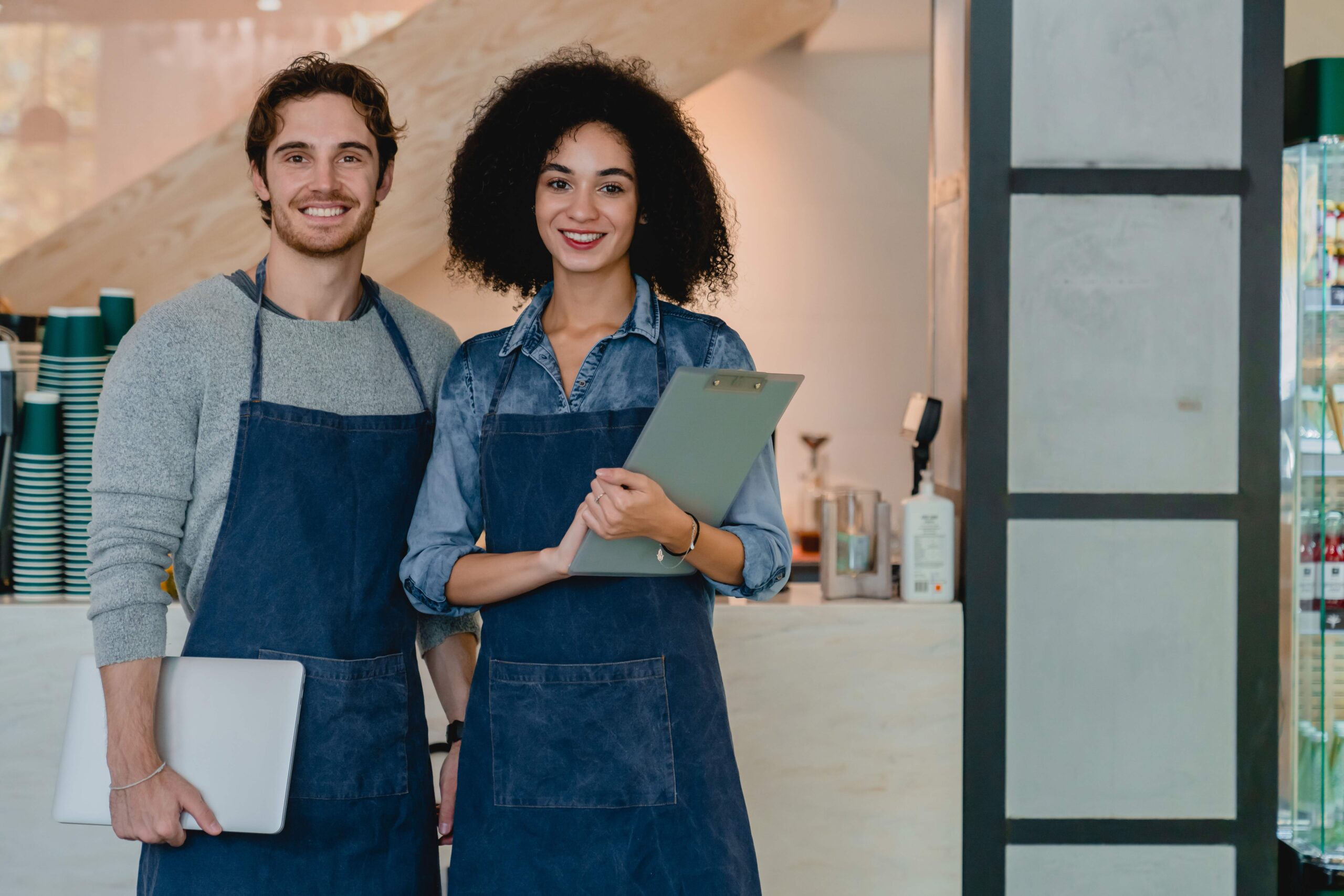 Implementación de protocolo familiar en pequeñas empresas de servicios. Pareja de emprendedores en su café sosteniendo una tablet y carpeta para organizar su protocolo familiar operativo.