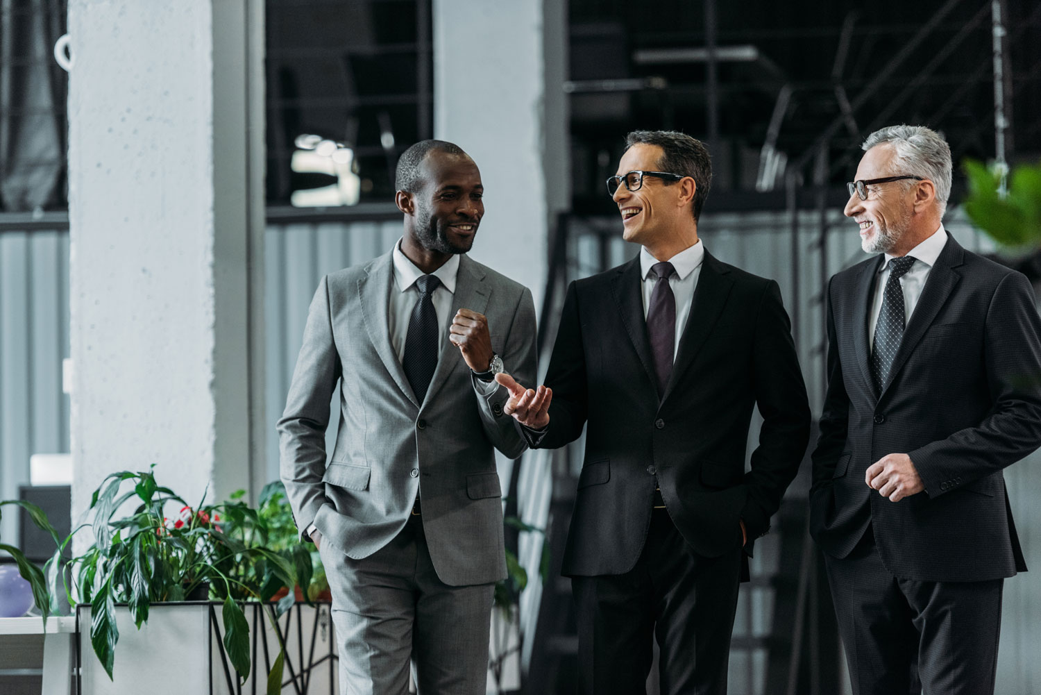 Claves de comunicación en la optimización de procesos empresariales Tres ejecutivos sonrientes conversando sobre la optimización de procesos empresariales en una oficina moderna